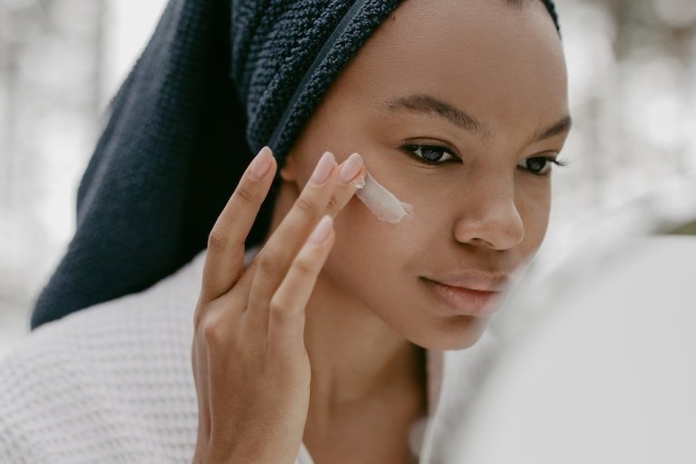 Woman in bathrobe applying face cream | Reflect Beauty